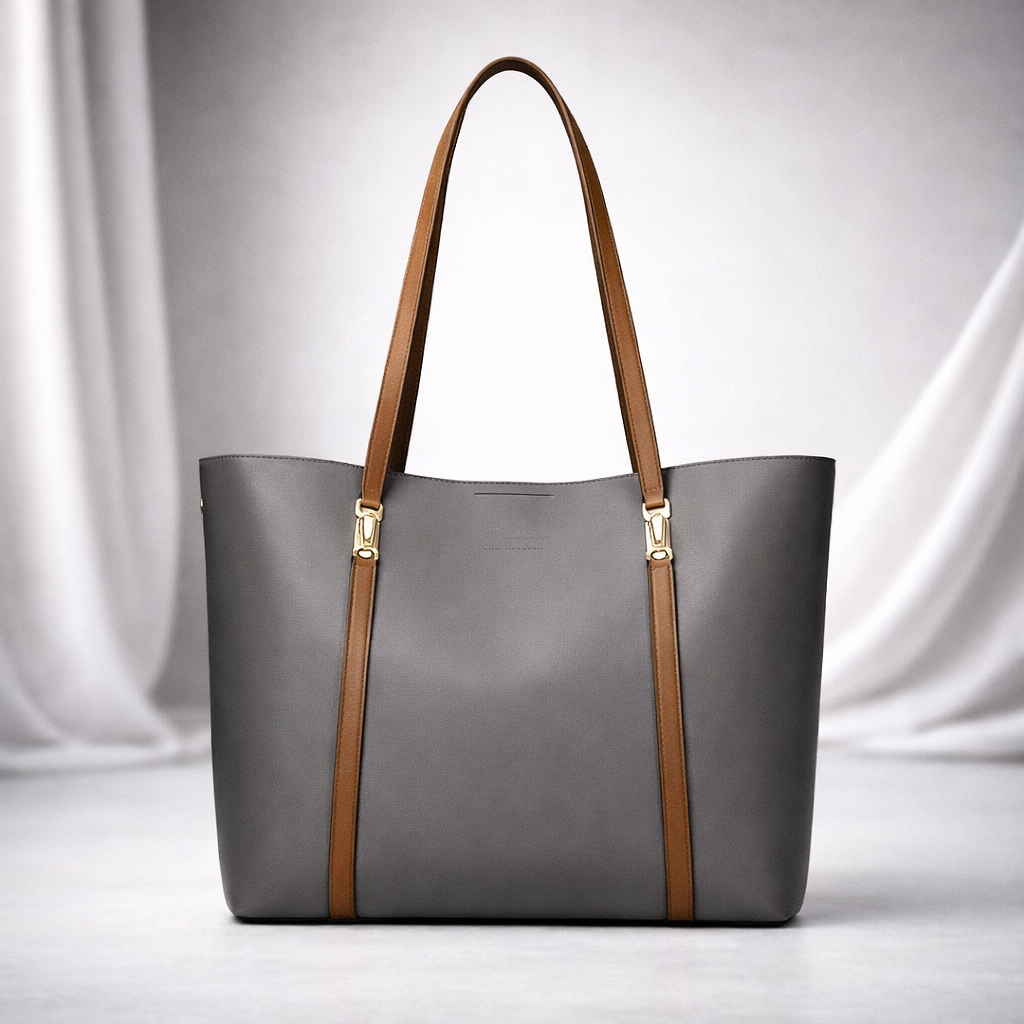 Gray leather women's tote bag with tan brown straps, gold hardware accents, displayed against white draped fabric background.