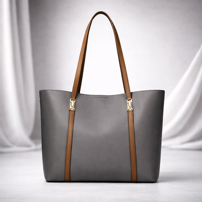 Gray leather women's tote bag with tan brown straps, gold hardware accents, displayed against white draped fabric background.