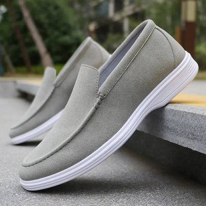 Gray suede slip-on loafers with white rubber sole displayed on concrete steps outdoors