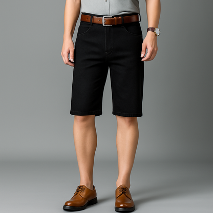 Men's black stretch denim shorts with brown leather belt and dress shoes, styled with gray shirt and watch.