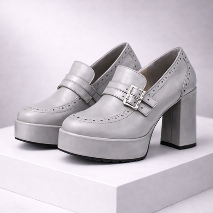 Silver platform block heel loafers with brogue detailing, double buckle strap, and chunky sole displayed on white stand.