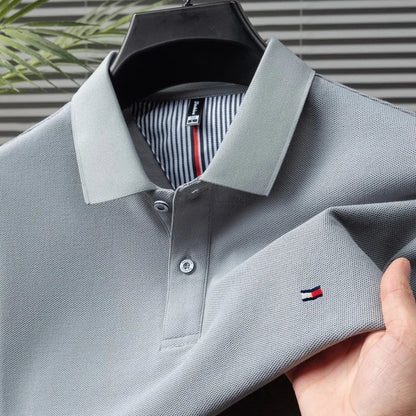Gray men's cotton polo shirt with Tommy Hilfiger logo, button placket, spread collar, and striped inner lining, on hanger.