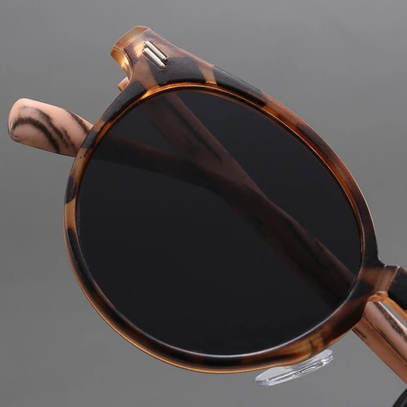 Round tortoiseshell sunglasses with dark gray lenses, brown patterned acetate frame, and silver rivets, shown from above.