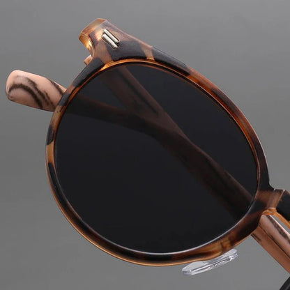 Round tortoiseshell sunglasses with dark gray lenses, brown patterned acetate frame, and silver rivets, shown from above.