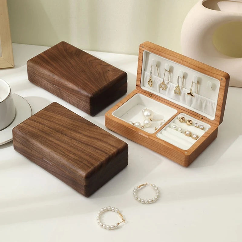 Wooden jewelry box organizer open displaying necklaces, earrings, and pearl hoops, with two closed boxes beside it.