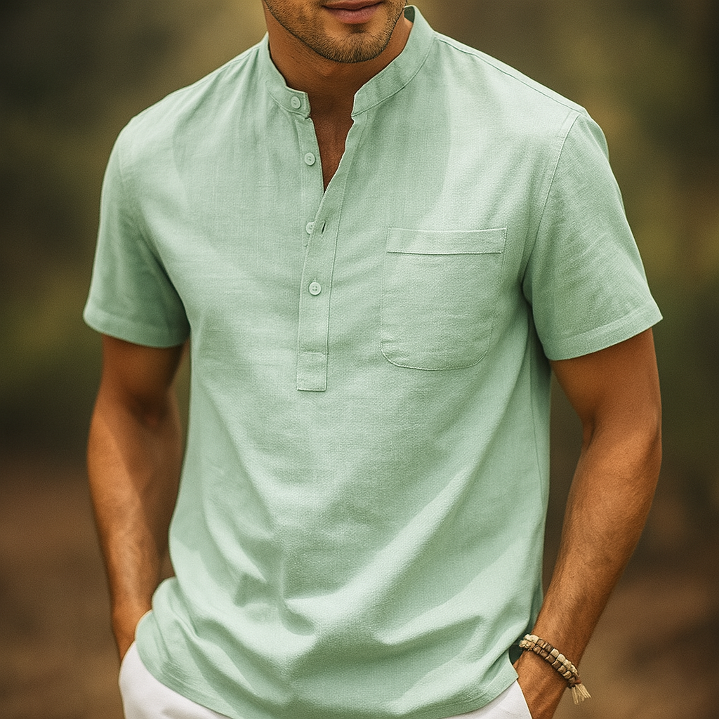 Men's light green linen band collar henley shirt with chest pocket and short sleeves, worn with white pants.