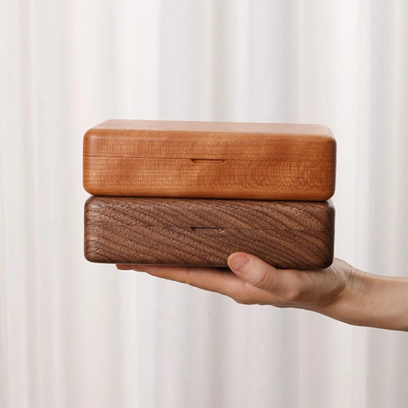Hand holding two stacked wooden jewelry boxes, one light cherry wood and one dark walnut, with hinged lids