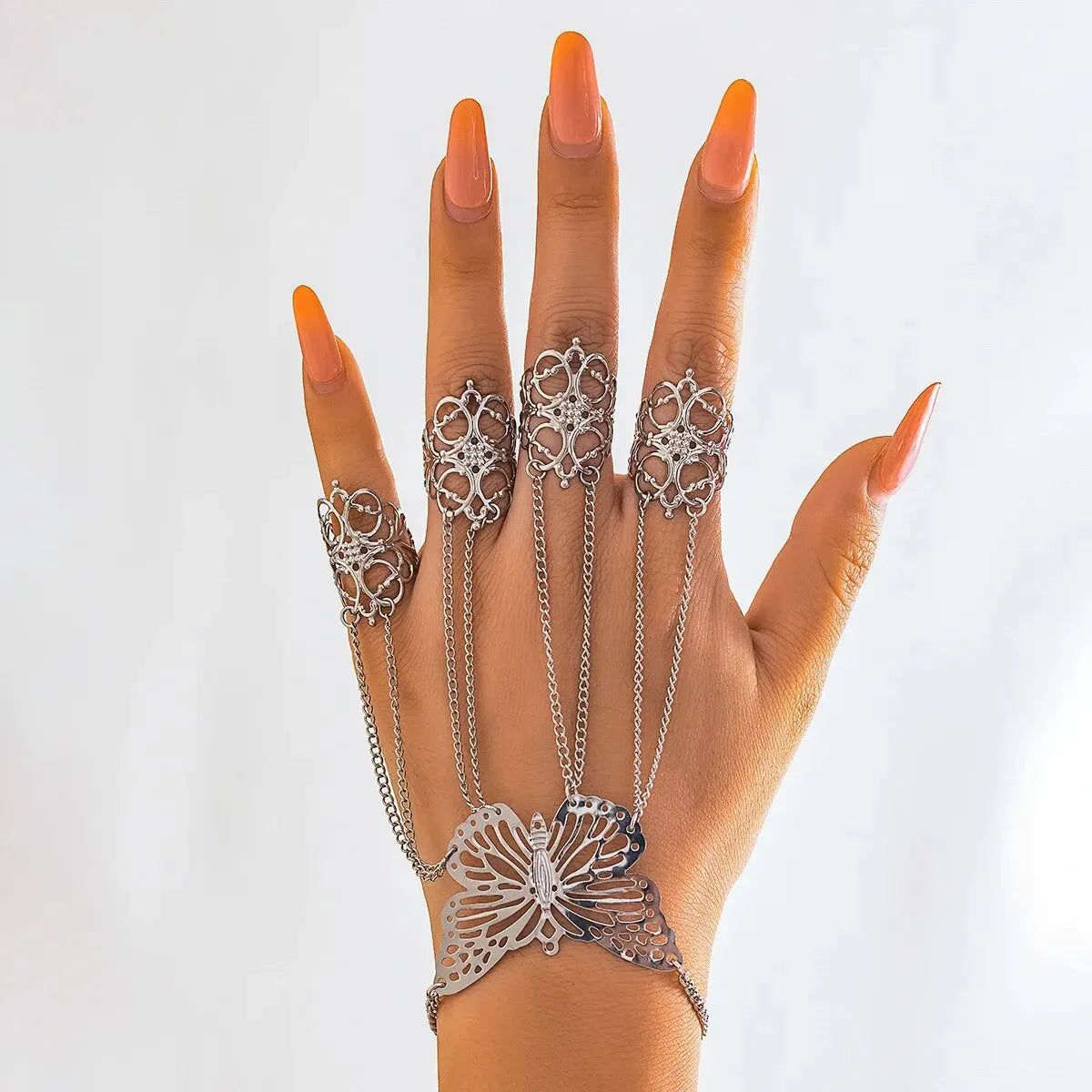 Silver butterfly bracelet connected by chains to four ornate filigree rings on a hand with orange nails