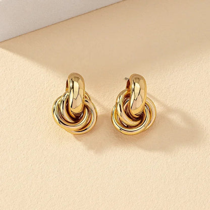 Gold tone interlocked knot hoop earrings for women on beige background, chunky twisted metal design statement jewelry