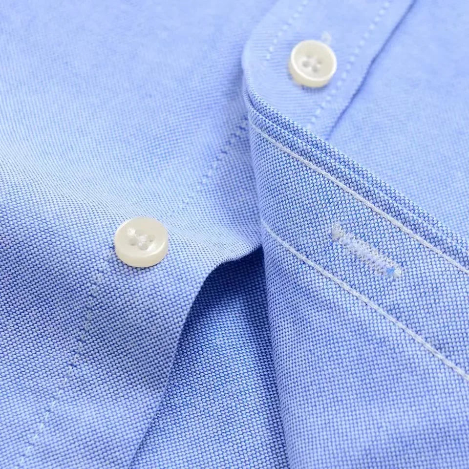 Close-up of a light blue men's cotton button-down shirt showing white four-hole buttons and fine Oxford weave fabric detail.