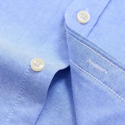 Close-up of a light blue men's cotton button-down shirt showing white four-hole buttons and fine Oxford weave fabric detail.