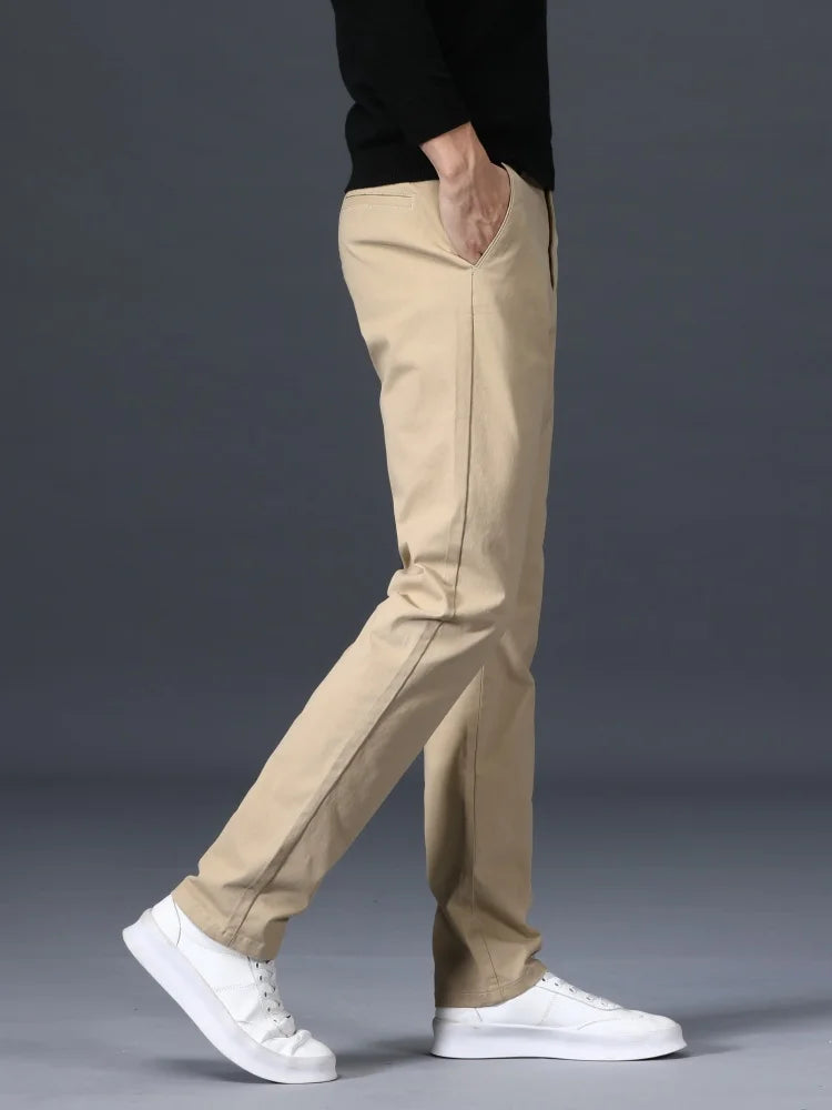 Man wearing slim-fit khaki cotton dress pants with a black top and white sneakers, side profile view.