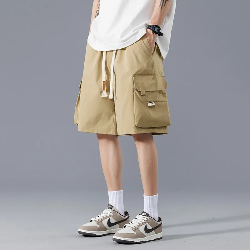 Men's khaki cargo shorts with drawstring waist and large side pockets, paired with white tee and Nike sneakers.