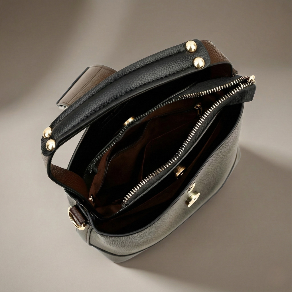Open black leather bucket handbag showing brown interior, gold stud hardware, zipper pocket, and adjustable shoulder strap.