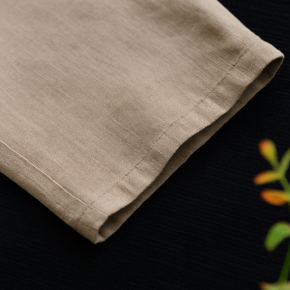 Close-up of beige linen tapered pants showing clean hemline stitching and natural fabric texture on dark background.