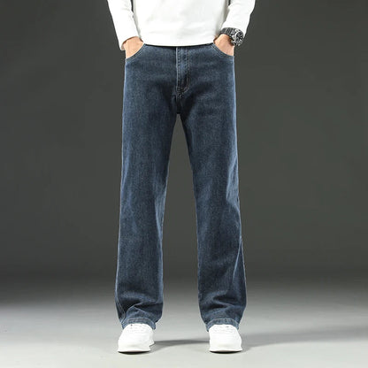 Men's straight leg stretch denim jeans in medium blue wash, worn with white sneakers and white long-sleeve shirt.