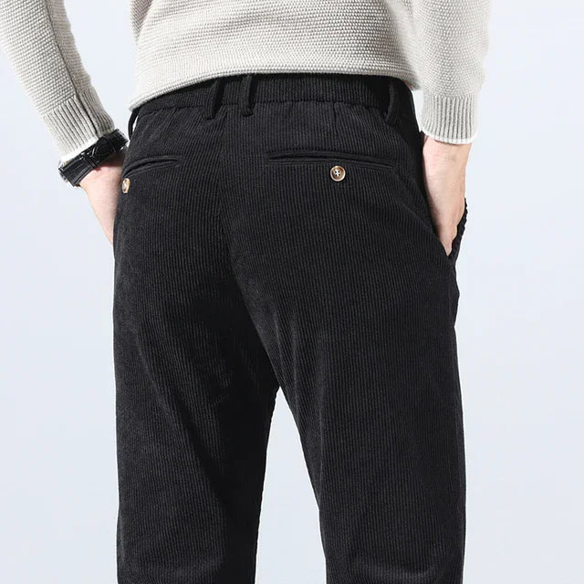 Man wearing black corduroy slim fit pants from behind, paired with a light gray knit sweater.