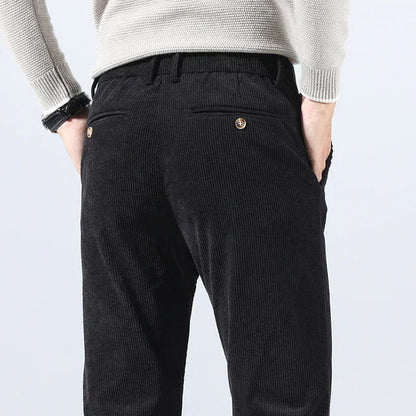 Man wearing black corduroy slim fit pants from behind, paired with a light gray knit sweater.