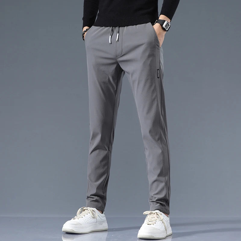 Men wearing slim-fit gray cotton drawstring joggers with side label detail, paired with white sneakers and black sweater.