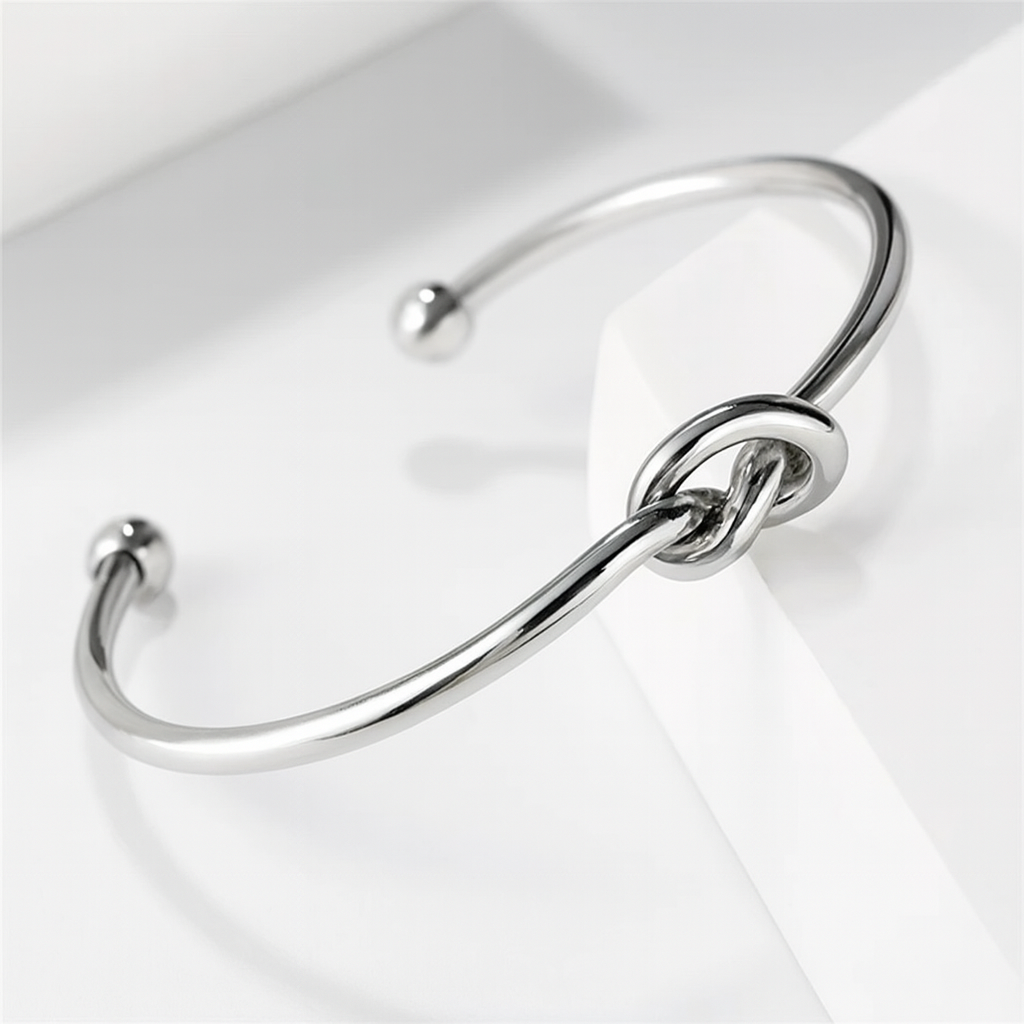 Silver open cuff bangle bracelet with decorative love knot centerpiece and ball-tip ends on white surface