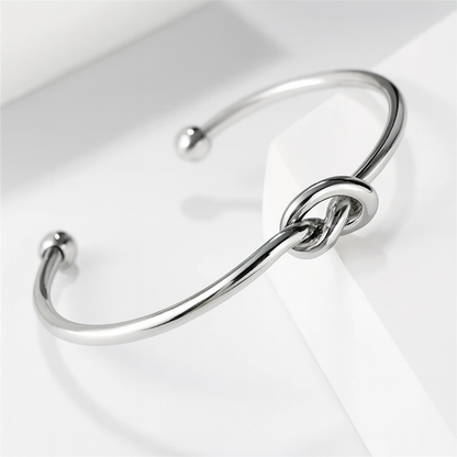 Silver open cuff bangle bracelet with decorative love knot centerpiece and ball-tip ends on white surface