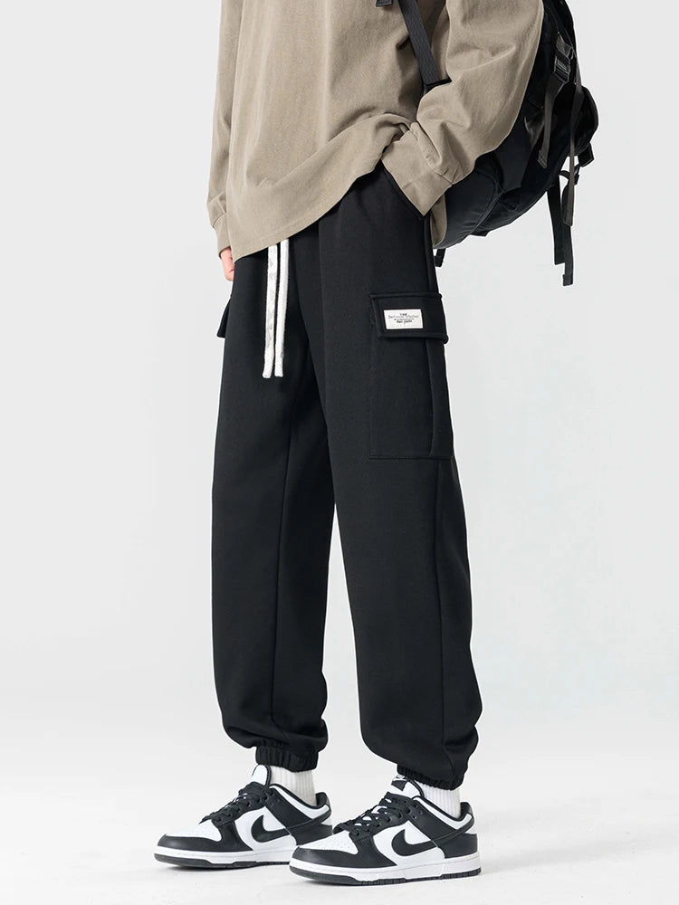 Black men's cargo jogger pants with drawstring waist, side pockets, label detail, paired with Nike Dunk Low sneakers.
