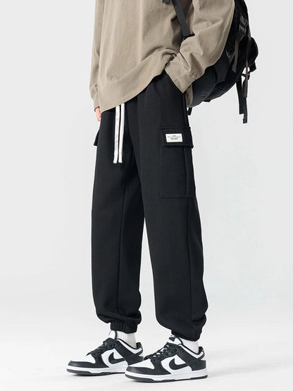 Black men's cargo jogger pants with drawstring waist, side pockets, label detail, paired with Nike Dunk Low sneakers.