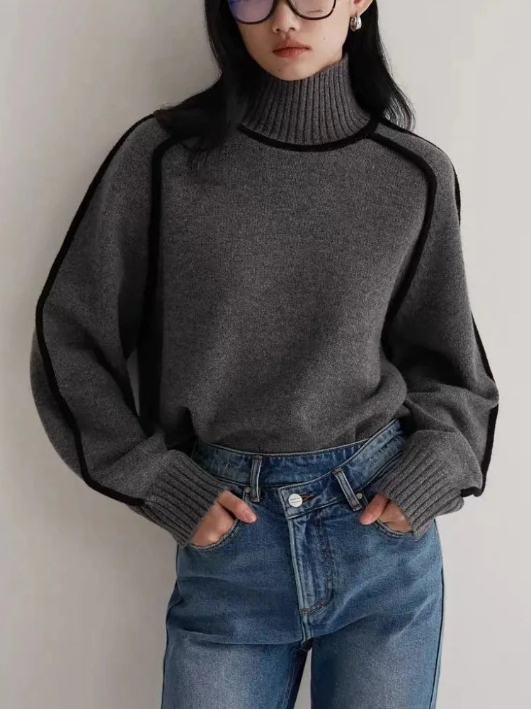 Gray women's turtleneck ribbed sweater with black contrast piping, styled with blue jeans and sunglasses.