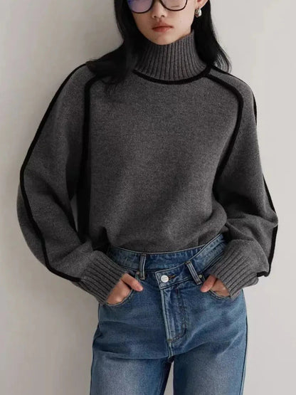 Gray women's turtleneck ribbed sweater with black contrast piping, styled with blue jeans and sunglasses.