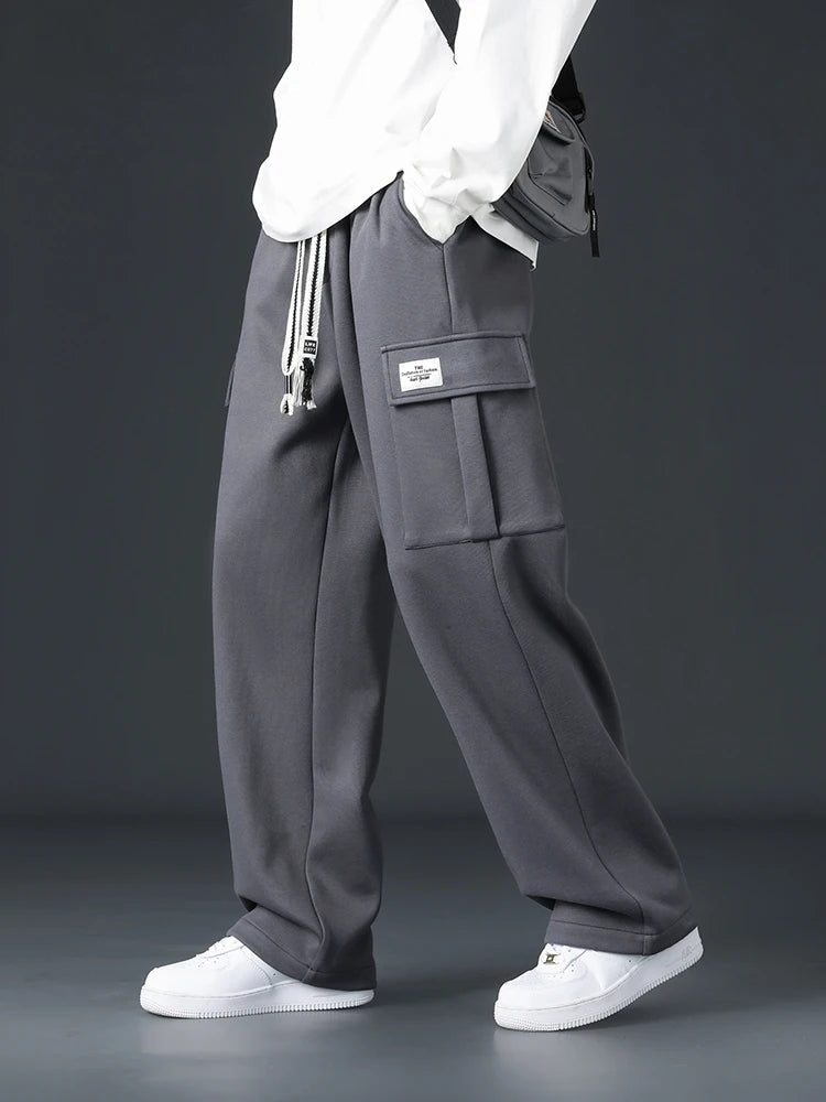 Men's gray wide-leg cargo sweatpants with drawstring waist, side patch pocket, worn with white sneakers and top.