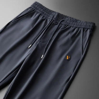Navy blue men's drawstring jogger pants with elastic waistband and orange V logo patch on left thigh