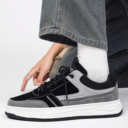 Men's black and gray patchwork low-top lace-up sneakers with white sole, worn with white socks and gray jeans.