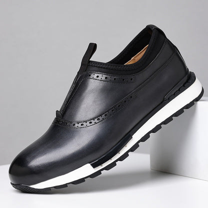 Black men's leather slip-on loafers with brogue detailing and white rubber sole on gray background