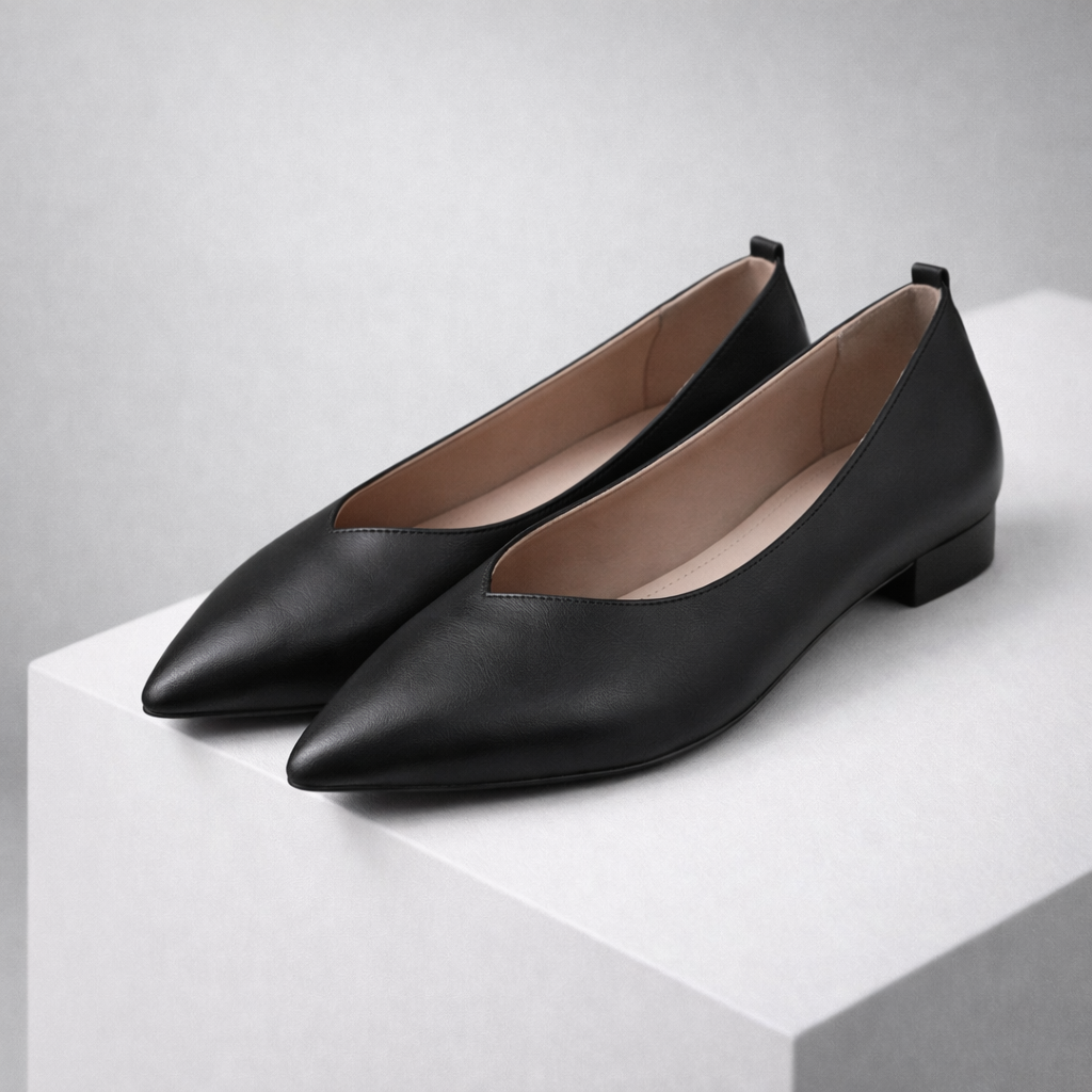 Black pointed-toe leather ballet flats with V-cut vamp, low block heel, and nude interior lining displayed on white surface.