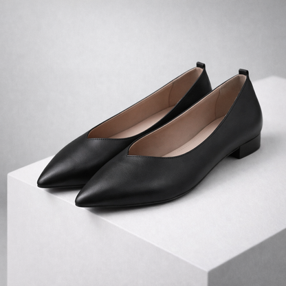 Black pointed-toe leather ballet flats with V-cut vamp, low block heel, and nude interior lining displayed on white surface.