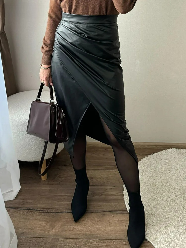 Black vegan leather wrap midi skirt with ruched detail and front slit, styled with brown sweater and black ankle boots