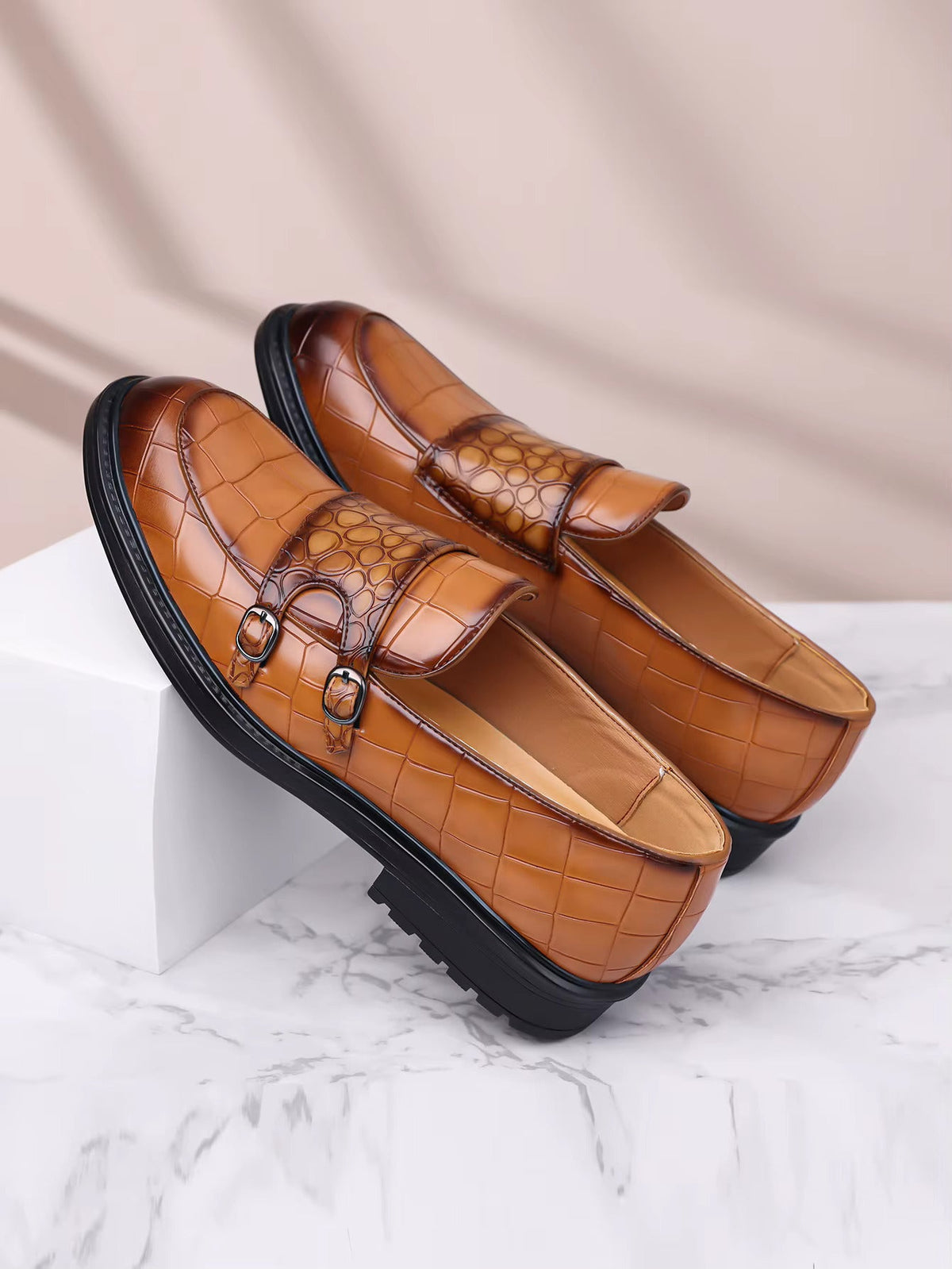 Tan croc-embossed leather men's loafers with double monk straps and chunky black rubber sole on marble surface.