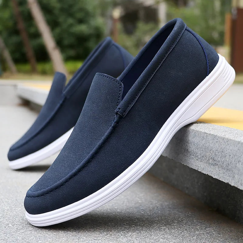 Navy blue suede slip-on loafers for men with white rubber sole, displayed on concrete steps outdoors
