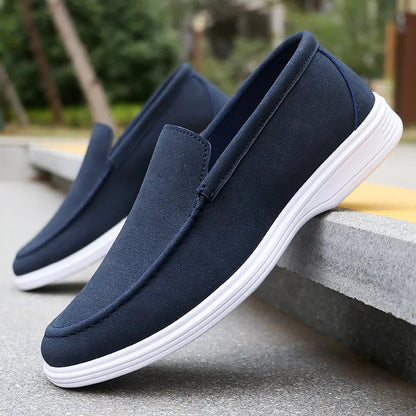 Navy blue suede slip-on loafers for men with white rubber sole, displayed on concrete steps outdoors
