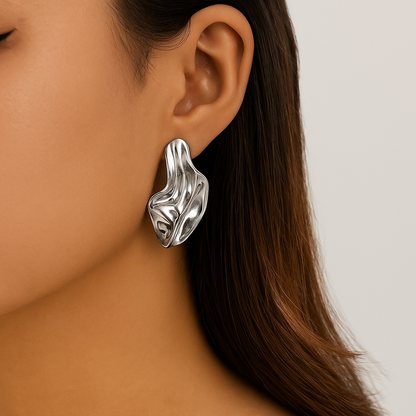Silver chunky twisted drop earrings with fluid sculptural design worn on model's ear, statement jewelry piece.