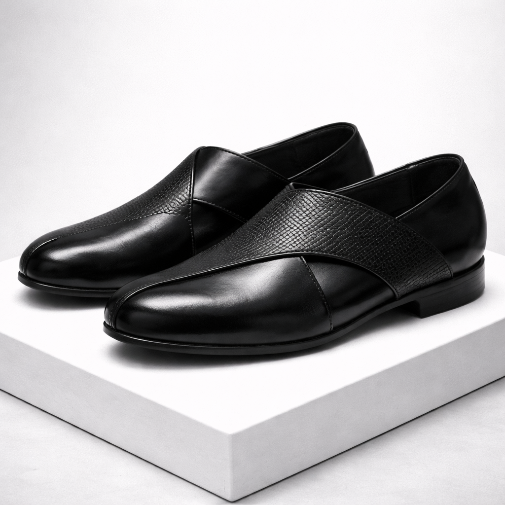 Black men's leather slip-on loafers featuring a cross strap design with textured and smooth leather panels, displayed on white platform.