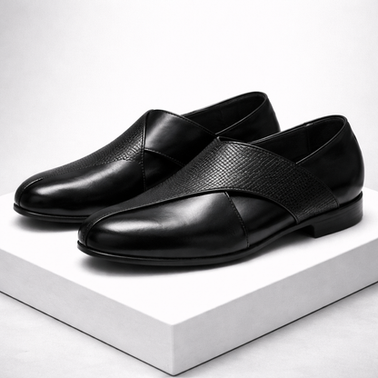 Black men's leather slip-on loafers featuring a cross strap design with textured and smooth leather panels, displayed on white platform.