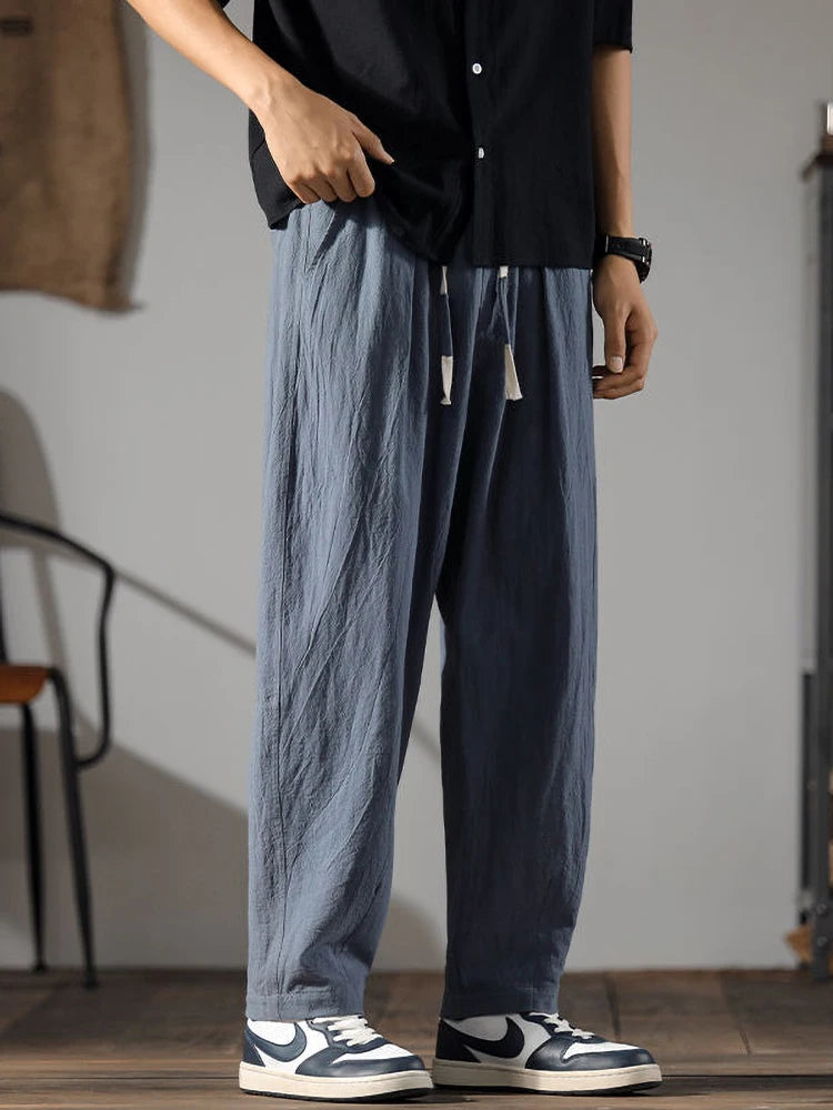 Men's wide-leg blue linen drawstring pants styled with black shirt and Nike sneakers, relaxed casual fit