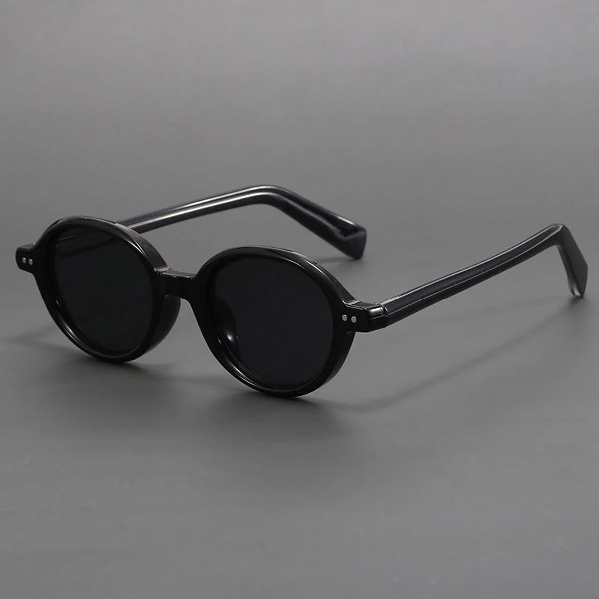 Black round frame sunglasses with thick acetate temples and dark lenses, displayed on gray background