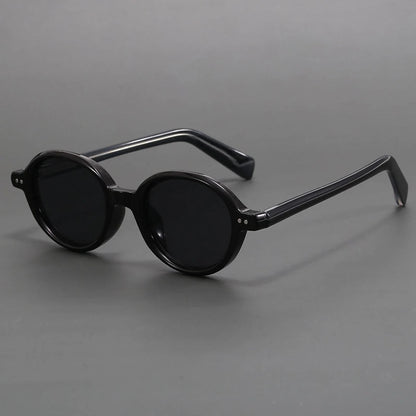 Black round frame sunglasses with thick acetate temples and dark lenses, displayed on gray background