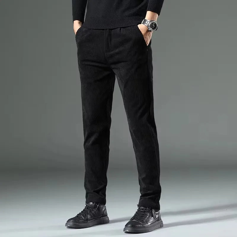 Black men's corduroy slim fit chino pants with elastic waist, styled with black sneakers and sweater.
