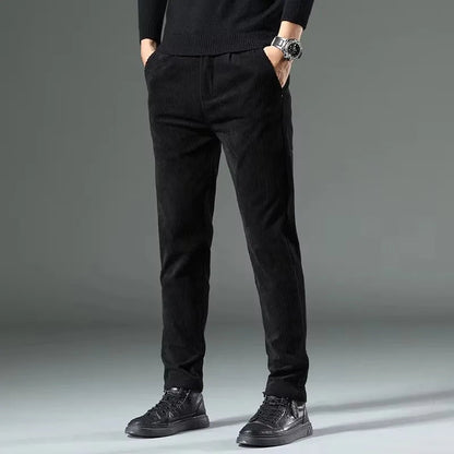 Black men's corduroy slim fit chino pants with elastic waist, styled with black sneakers and sweater.